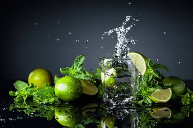 Limonlu ve naneli iç, siyah yansıtıcı arka planda. Limon dilimi bardağa dökülür..