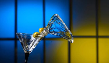 Bardakta martini ve yeşil zeytin. Renkli bir arkaplanda sıçramalar. Boşluğu kopyala.