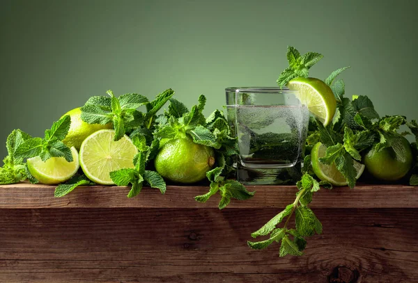 Carbonated drink or cocktail with limes and mint on a old wooden table. Green background.
