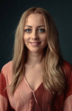 Dost canlısı, gülümseyen sarışın kameraya bakıyor. Karanlık bir arka planda 30 yaşında bir kadının portresi..