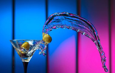 Bardakta martini ve yeşil zeytin. Renkli bir arkaplanda sıçramalar. Boşluğu kopyala.