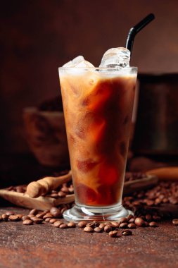 İçine krema dökülen buzlu kahve içkinin dokusunu ve ferahlatıcı bakışını gösteriyor. Mutfak gereçleri ile eski kahverengi bir masada donmuş bardak ve kahve çekirdekleri. Boşluğu kopyala.