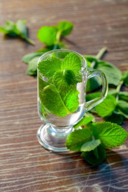 Bahçedeki eski ahşap bir masada nane çayı. Taze yeşil dallar ve sıcak çayla birlikte bardak..