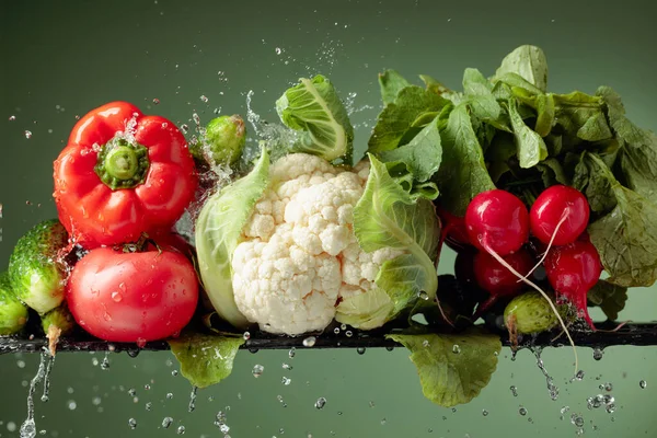 Various raw vegetables with water splash. Cauliflower, tomato, cucumber, radish and paprika on a green background.