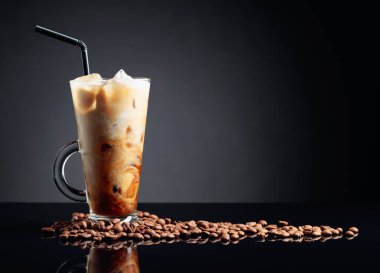 Siyah yansıtıcı arka planda buzlu kahve. İçine krema dökülüyor. İçkinin dokusunu ve ferahlatıcı görünüşünü gösteriyor. Boşluğu kopyala.