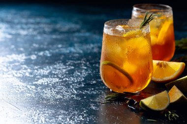 Limonlu, limonlu ve biberiye dallarıyla süslenmiş geleneksel buzlu çay. Koyu mavi bir masada turunçgil dilimli donmuş bardaklar. Boşluğu kopyala.