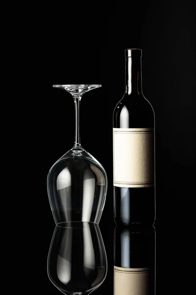 黒を基調とした赤ワインと反転ワイングラスのボトル ボトルに古い空のラベルがあります ワイン造りの概念 — ストック写真
