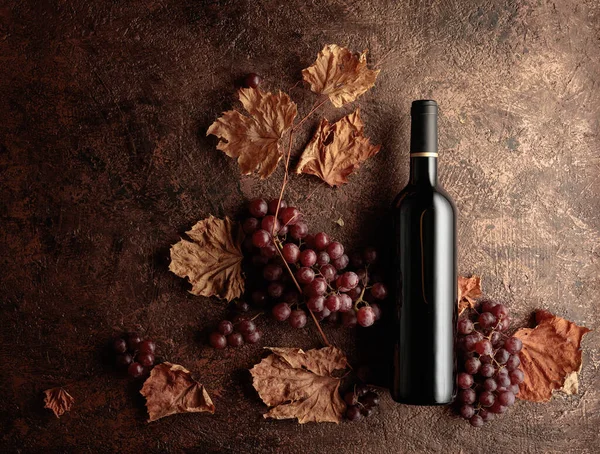 Bottle of red wine with ripe grapes and dried up vine leaves. Old copper background.  Copy space, top view.