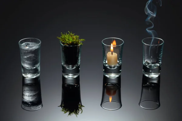 Four elements of nature - air, fire,  earth, water. Four elements concept in glasses on a black reflective background.