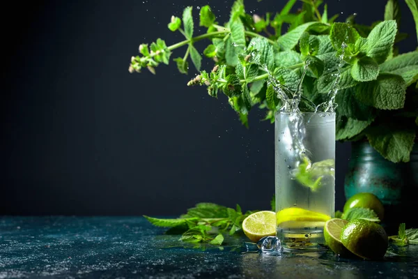 Buzlar mojito ile birlikte cam parçalarına düşer. Limonlu, naneli ve buzlu yaz içeceği. Kopyalama alanı olan koyu arkaplan.