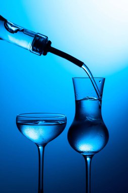 Votka şişeden buzlu dondurulmuş bardaklara dökülür. Mavi arka planda donmuş bardaklar.