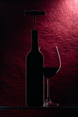 Tirbuşonlu şişe ve koyu kırmızı arka planda bir bardak kırmızı şarap..