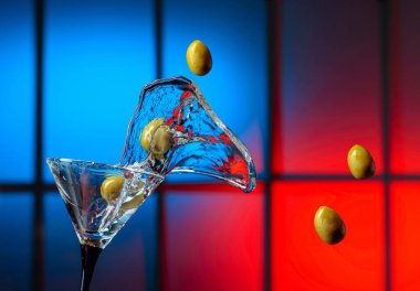Bardakta martini ve yeşil zeytin. Renkli bir arkaplanda sıçramalar. Boşluğu kopyala.