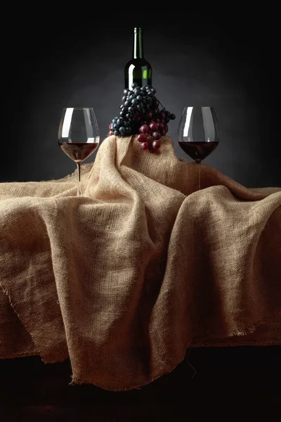 Red wine and grapes on a table covered with burlap.