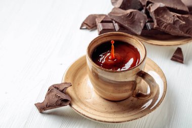 Beyaz ahşap bir masada sıcak çikolata ve kırık çikolata parçaları. Bir damla içki bardağa düşer. Boşluğu kopyala.