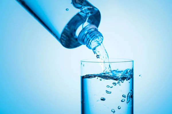 stock image Pouring water from a bottle into glass on a blue background. Copy space.