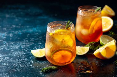 Limonlu buzlu çay, limon ve biberiyeyle süslenmiş buz. Koyu mavi bir masada turunçgil dilimli donmuş bardaklar. Boşluğu kopyala.