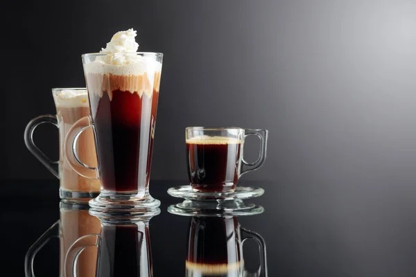 Espresso, Irish coffee, and latte on a black reflective background. Copy space.