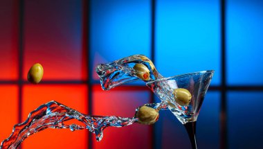 Bardakta martini ve yeşil zeytin. Renkli bir arkaplanda sıçramalar. Boşluğu kopyala.