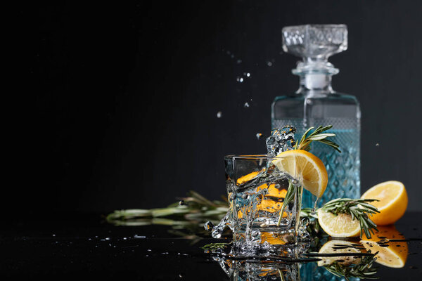 Gin-tonic with lemon slices and twigs of rosemary. Piece of ice falls into the glass. Copy space.