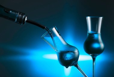 Alkollü içeceği buzlu bardağa dolduruyorum. Mavi arka planda buzlu bardaklarda güçlü alkollü içecekler. Boşluğu kopyala.