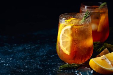 Limonlu, limonlu ve biberiye dallarıyla süslenmiş geleneksel buzlu çay. Koyu mavi bir masada turunçgil dilimli donmuş bardaklar. Boşluğu kopyala.