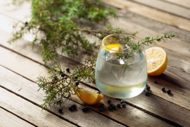 Limonlu alkol içeceği (cin tonik kokteyli), ardıç dalı ve kırsal ahşap masa üzerindeki buz, kopyalama alanı. Limon ve ardıç meyveli buzlu kokteyl..