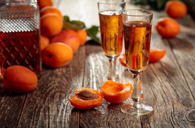 Kayısı likörü ve taze kayısılar eski bir ahşap masada. Kırsal bir arka planda şarap ve sulu meyveler. 