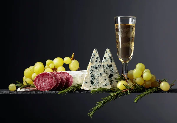 黒を基調とした白ワインと軽食 ワイン ブルーチーズ 乾燥したソーセージ ブドウ ローズマリーのガラス シンプルでおいしい食べ物 スペースのコピー — ストック写真