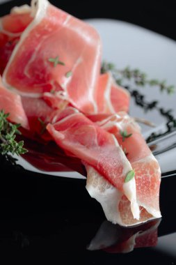 Siyah tabakta kekik olan bir Prosciutto. Siyah yansıtıcı arkaplan.