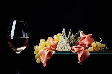 Atıştırmalıklı beyaz şarap. Mavi peynirli üzümler, siyah arka planda prosciutto ve kekik. Boşluğu kopyala.