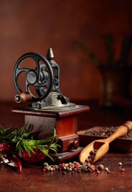 Çeşitli biber ve baharatlı klasik biber değirmeni. Kahverengi arka planda mutfak aletleri, baharatlar ve biberiye olan eski biber değirmeni.