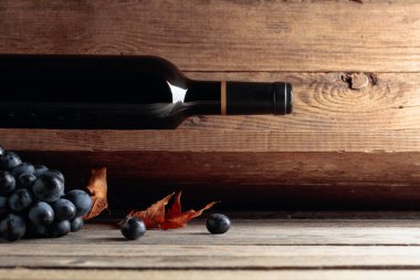 Şarap mahzenindeki eski ahşap bir masada bir şişe kırmızı şarap ve bir demet üzüm. Seçici odak.