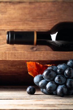 Şarap mahzenindeki eski ahşap bir masada bir şişe kırmızı şarap ve bir demet üzüm. Seçici odak.