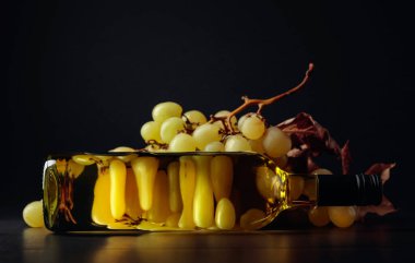 Kurumuş yapraklı olgun üzümler ve siyah arka planda kapalı bir şişe beyaz şarap.. 