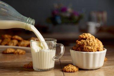 Mutfak masasında yulaflı kurabiye ve süt. Süt şişeden cam bardağa dökülür. Boşluğu kopyala.