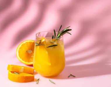 Turuncu, biberiye ve buzlu yaz kokteyli. Pembe arka planda, palmiye yaprağı gölgesiyle iç. Yaz, tropikal, taze kokteyl konsepti.