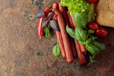 İnce tütsülenmiş sosis, eski bir kesim tahtasının üzerinde ekmek ve yeşillik. Üst görünüm, alanı kopyala.