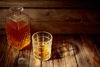 Zarif viski bardağı ve kehribar sıvısıyla dolu sürahi eski bir ahşap masada. Boşluğu kopyala.