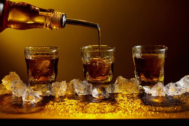 Viski şişeden cama doluyor. Viski ve buz siyah bir masada. Sarı ışık güzel gölgeler yaratır. Boşluğu kopyala.