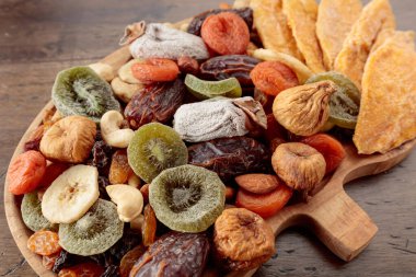 Kurutulmuş mango dilimleri, tropikal meyveler, fındıklar ve kuru üzümler eski ahşap bir masada. Üst görünüm.