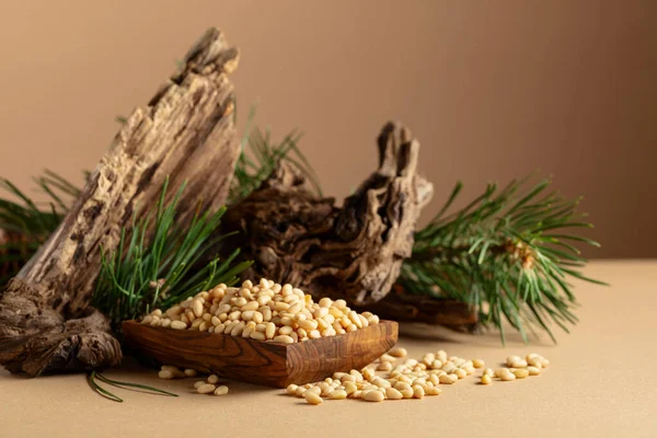 Çam fıstığı soyulmuş, sedir ağacı kurumuş ve yeşil dalları var. Bej bir arka planda ahşap tabakta çam fıstığı.