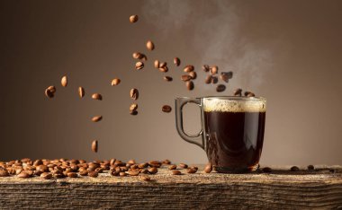 Eski ahşap bir masada cam bardakta espresso. Kavrulmuş kahve çekirdekleri hareket halinde. Boşluğu kopyala.