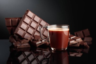 Bir bardak sıcak çikolata ve kırık acı çikolata. Kopyalama alanı olan siyah yansıtıcı arkaplan.