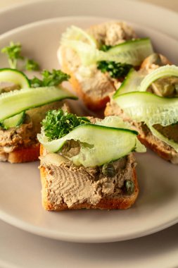 Pate, taze salatalık, kapari ve maydanozlu sandviç. Bej arkaplanda ezmeli tostlar.