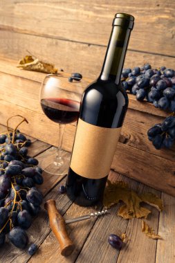 Eski ahşap bir masada bir şişe kırmızı şarap ve mavi üzüm. Eski boş bir şişede. Boşluğu kopyala.