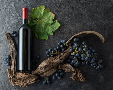 Bir şişe kırmızı şarap, mavi üzüm ve siyah taşlı arka planda eski asma parçaları. Üst Manzara. Boşluğu kopyala.
