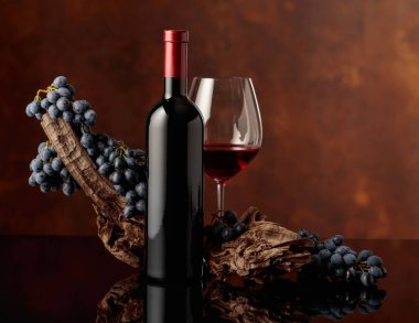 Kırmızı şarap, siyah yansıtıcı arka planda bir şişenin yanındaki bardağa döküldü. Kırmızı şarap, eskimiş bir pürüz ve kahverengi bir arka planda mavi üzümler..