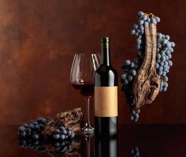 Kırmızı şarap, siyah yansıtıcı arka planda bir şişenin yanındaki bardağa döküldü. Kırmızı şarap, yıpranmış bir pürüz ve kahverengi arka planda mavi üzümler. Boş yeri olan eski bir şişe etiketinde.