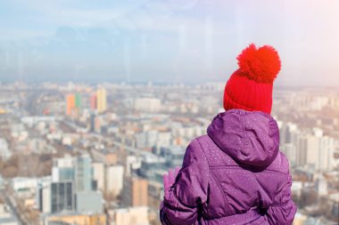 Uzun bir örgü bir ponpon ile mor şapkalı güzel bir genç kızla gülümsüyor ve şehrin yukarıdan bakar